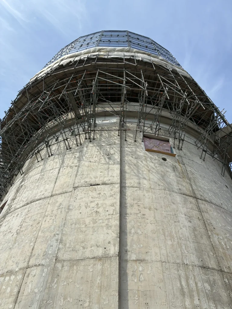 Betonnen silo op Zeeburgereiland in de steigers tijdens de verbouwing, van onderaf tegen een blauwe lucht.